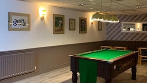 Une table de billard dans une pièce dotée d’un plancher en bois, d’un radiateur et de luminaires fixés au mur.