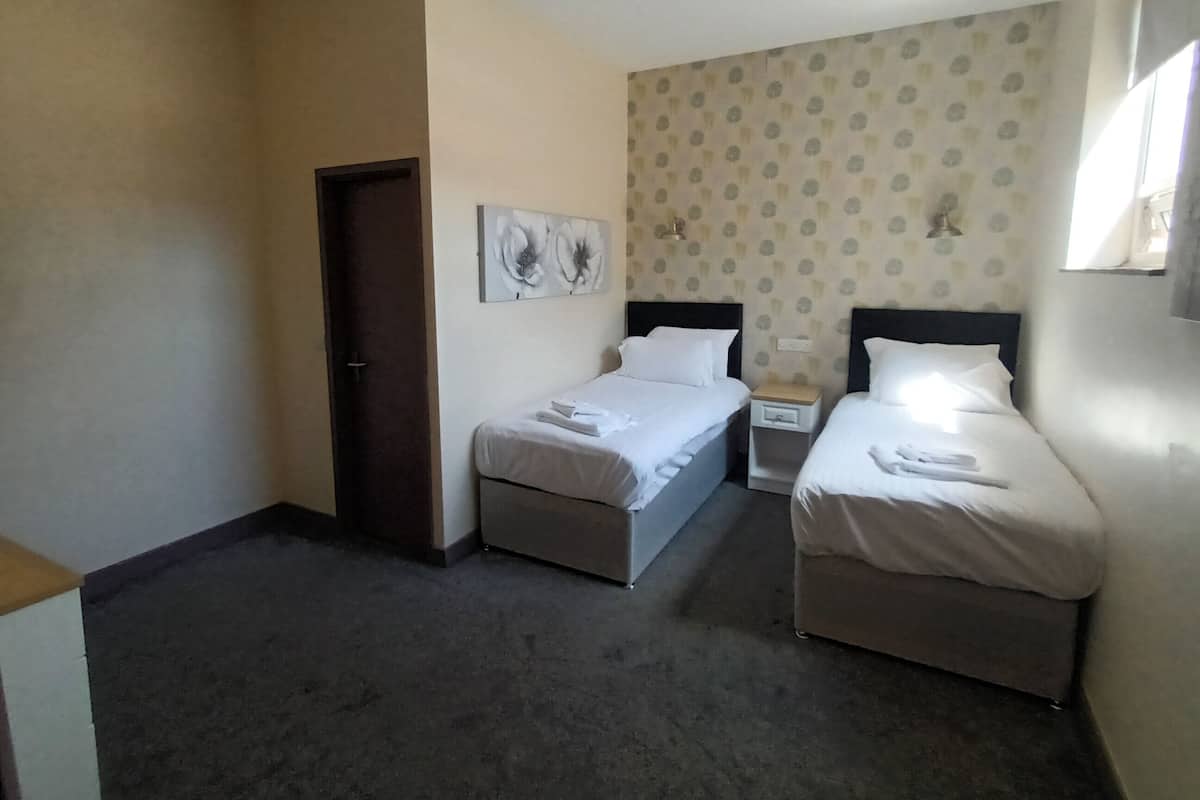 A hotel room with two single beds, a small bedside table with a lamp, and a door.