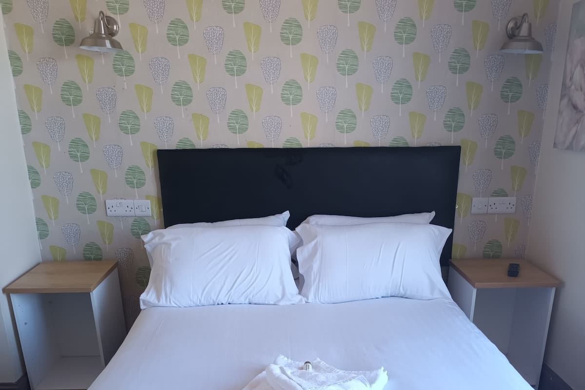 A neatly made bed with white linens, two pillows, and a folded towel on a large bed in a hotel room.