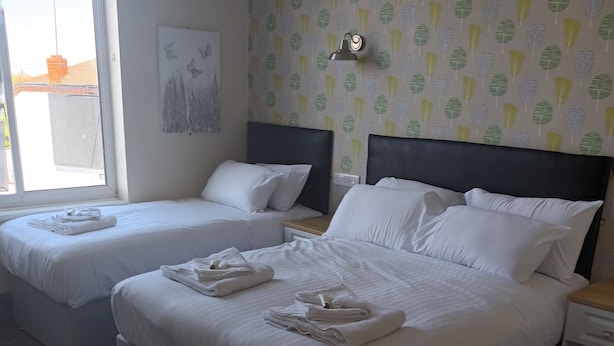 Une chambre d’hôtel avec deux lits, une table de chevet, une lampe et une fenêtre donnant sur l’extérieur.