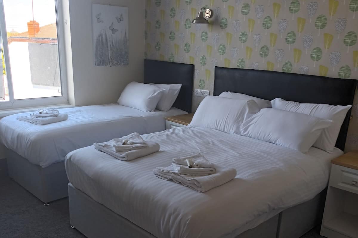 A hotel room with two beds, a nightstand, a lamp, and a window with a view of the outside.