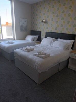 A hotel room with two beds, a nightstand, a lamp, and a window with a view of the outside. - The Saltley Inn (Birmingham)