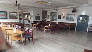 Un restaurant spacieux avec des tables et des chaises en bois, un coin bar et divers tableaux encadrés qui ornent les murs.