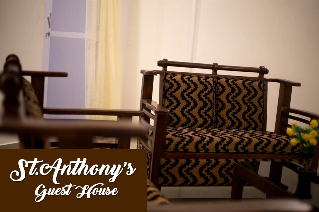 Une chaise en bois avec un coussin à motifs, dans une pièce où l’on aperçoit une porte et un vase rempli de fleurs jaunes.
