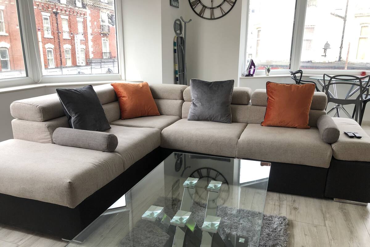 A modern living room with a sectional sofa, a glass coffee table, and a view of the city through large windows.
