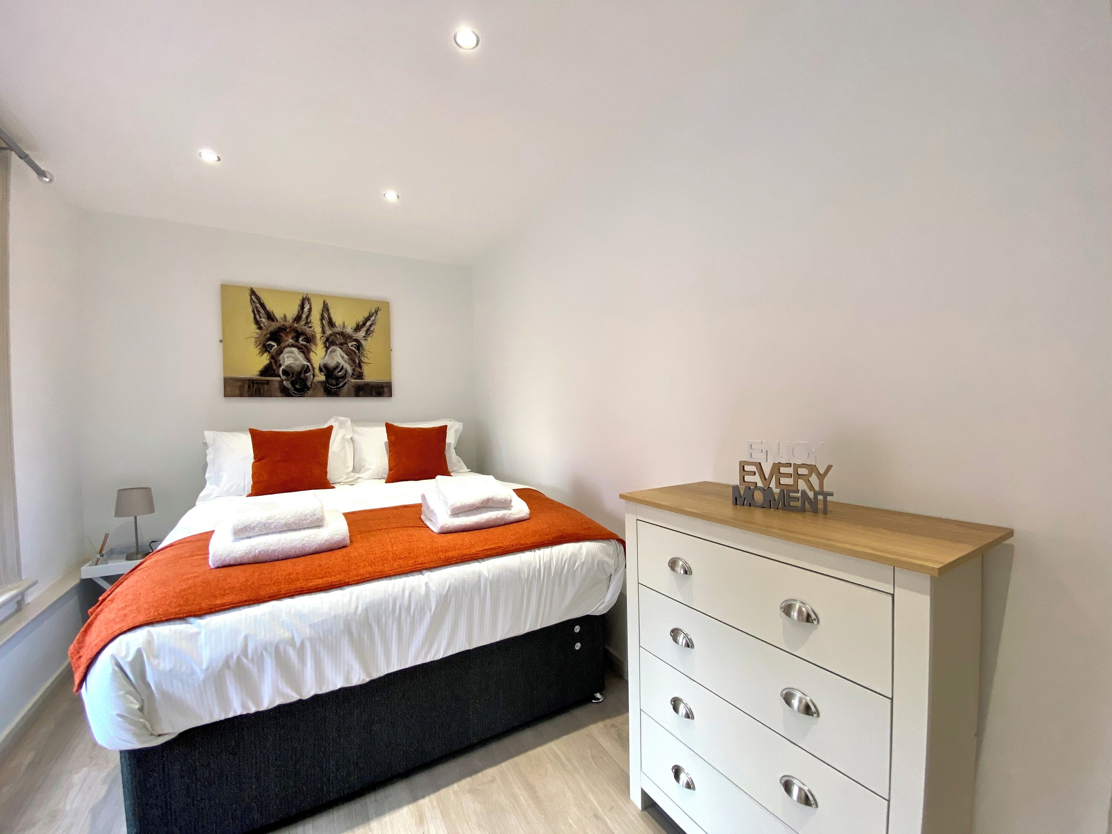 Ein modernes Schlafzimmer mit Bett, Nachttisch, Kommode und einem Wandbild.