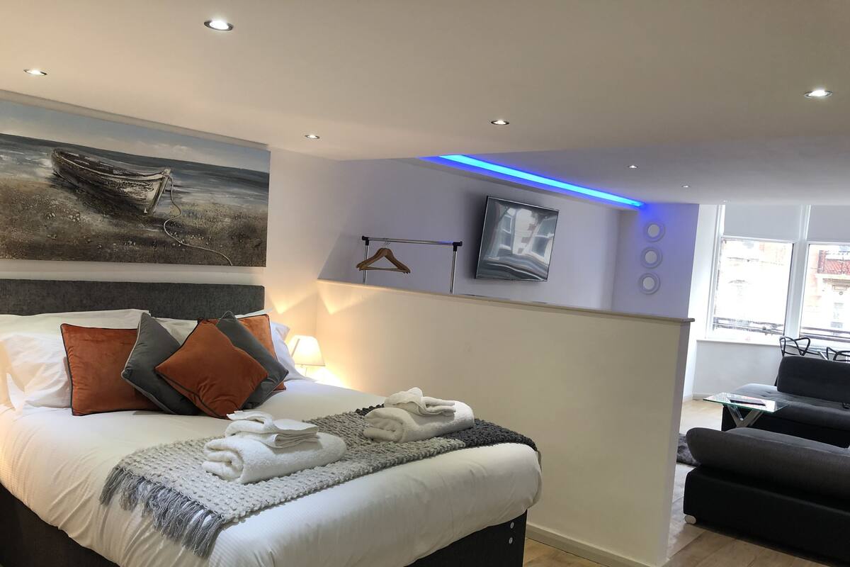 A modern hotel room with a large bed, a painting of a boat on the wall, a TV, and a sofa.