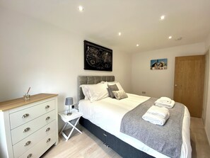 A modern bedroom with a bed, bedside table, and a dresser. - Princess Service Apartments - Town Centre (Blackpool)