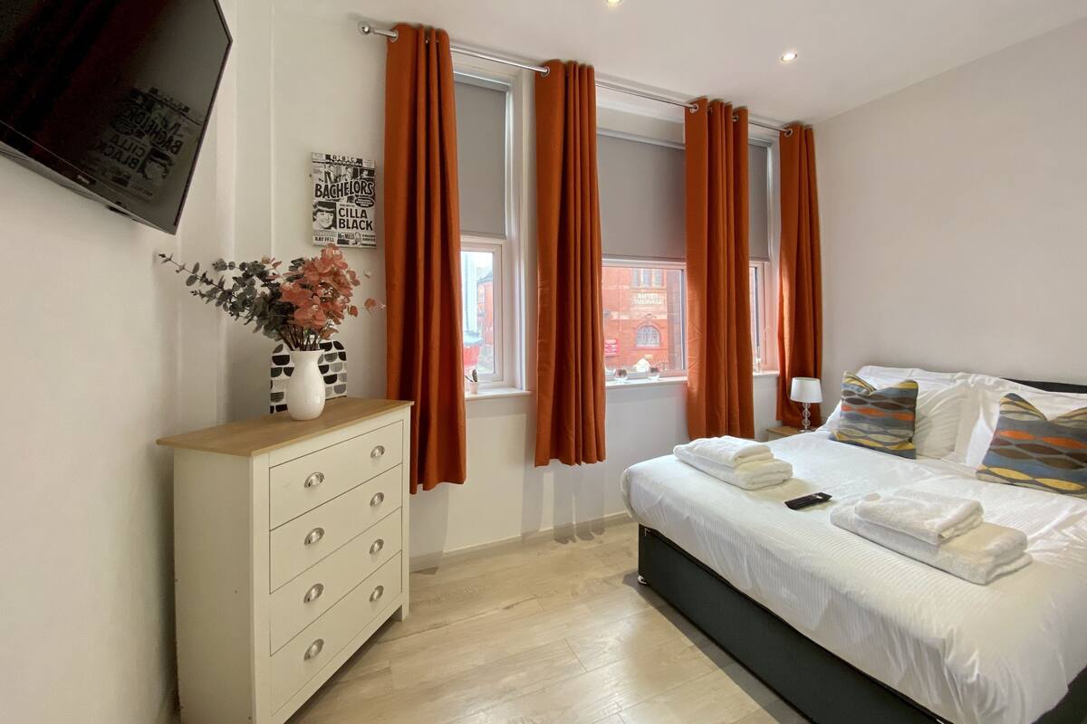 A bedroom with a bed, dresser, and windows with curtains.