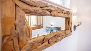 A rustic mirror with a natural wood frame mounted on a white wall, reflecting a staircase and a painting.