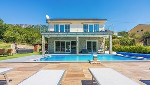 A two-story house with a swimming pool, outdoor seating, and a balcony.