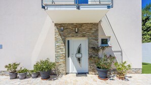 A modern building with a stone facade, a white door, and potted plants in front.