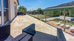 A balcony with outdoor seating and a view of a parking area and greenery.