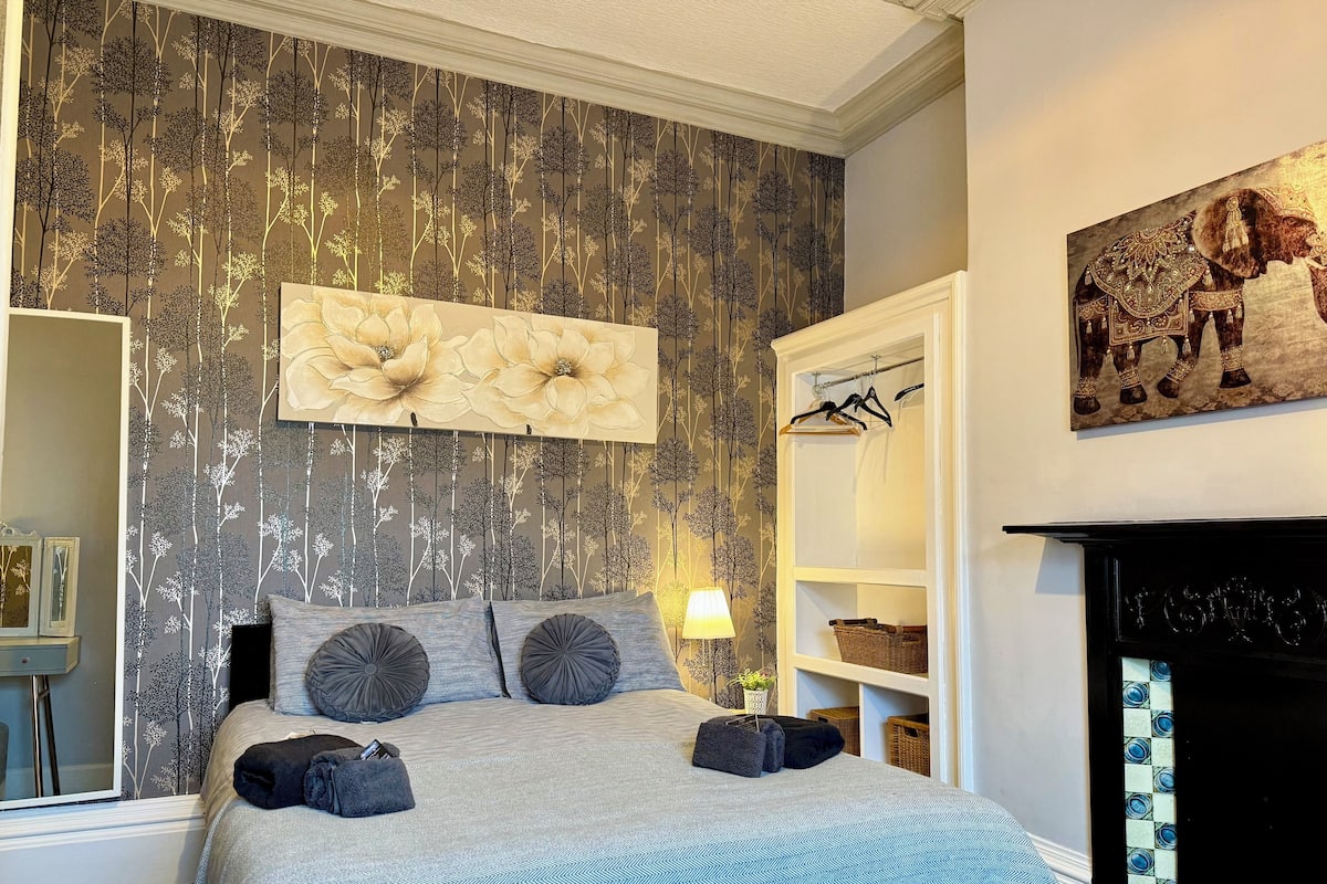 Une chambre à coucher avec un lit, une lampe fixée au mur, une cheminée et une bibliothèque.
