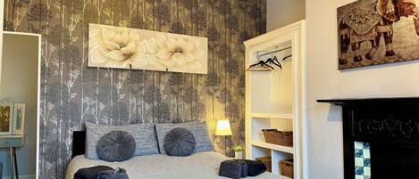 A bedroom with a bed, a wall-mounted lamp, a fireplace, and a bookshelf.