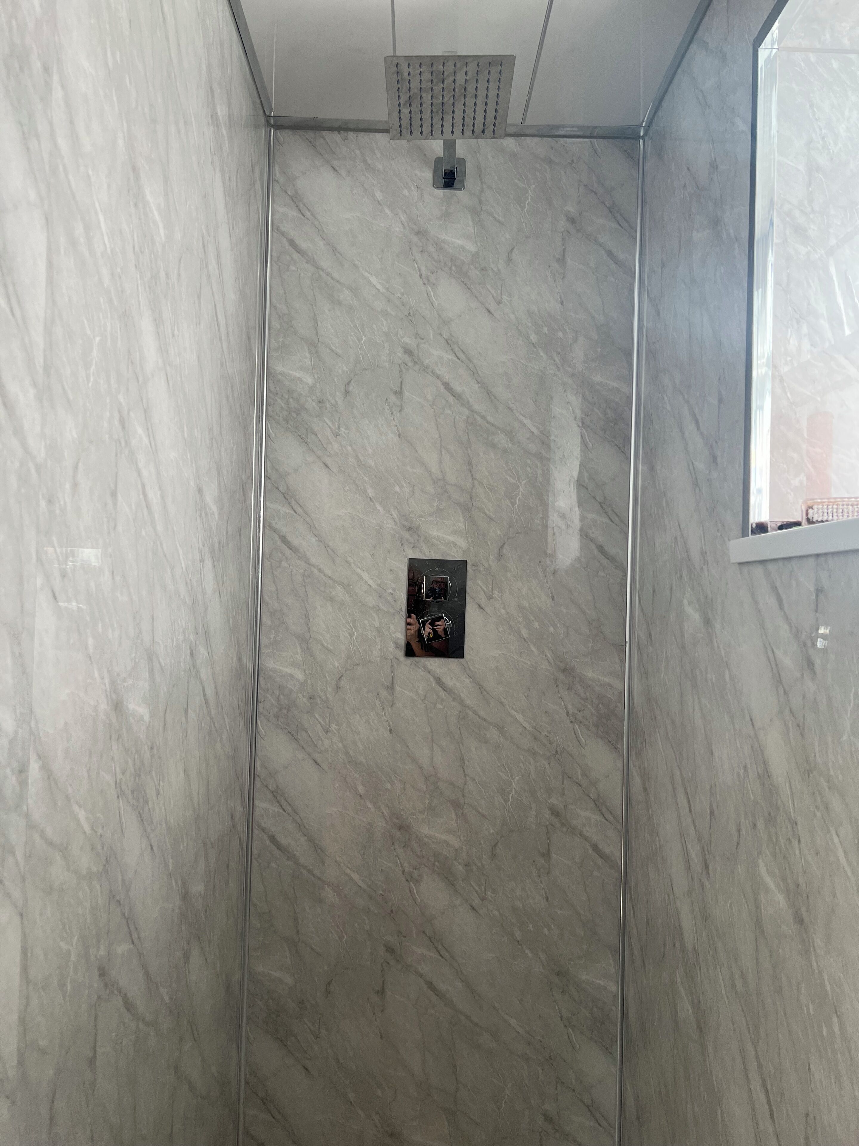 A shower with a marble wall and a small control panel.