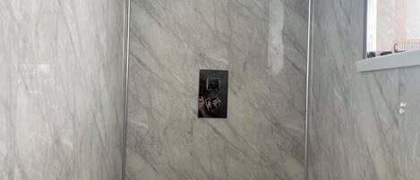 A shower with a marble wall and a small control panel.