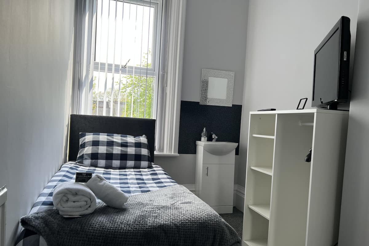 Une chambre à coucher comprenant un lit, une table de chevet, une télévision, une armoire et une fenêtre avec des rideaux.