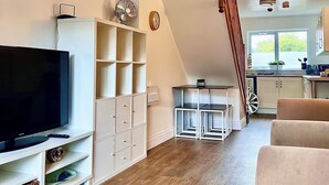A modern living room with a flat-screen TV, white shelving, and a staircase leading to a kitchen area. - St Andrews House Hotel (Preston)