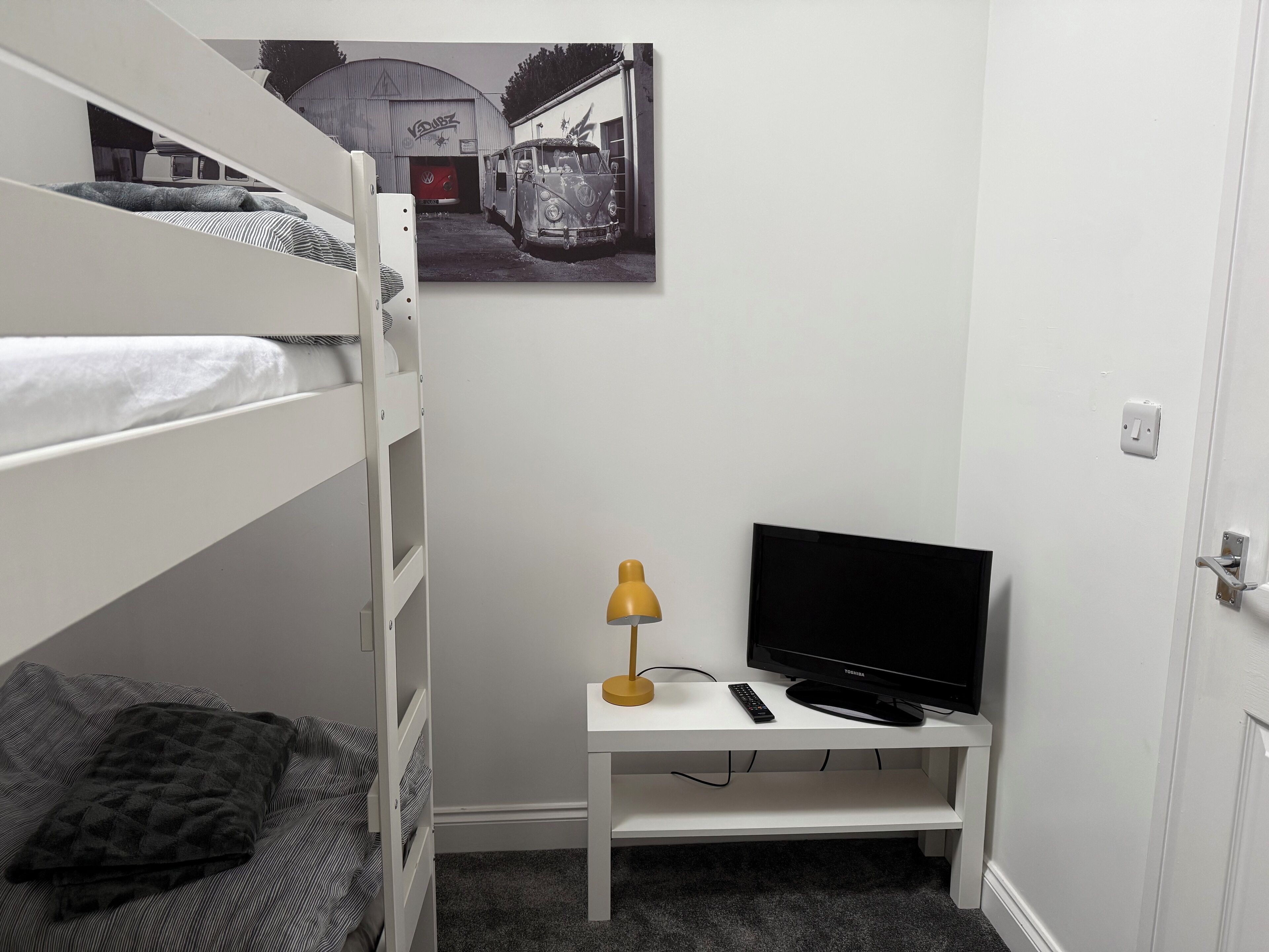 A bedroom with bunk beds, a desk with a TV, a lamp, and a blanket.