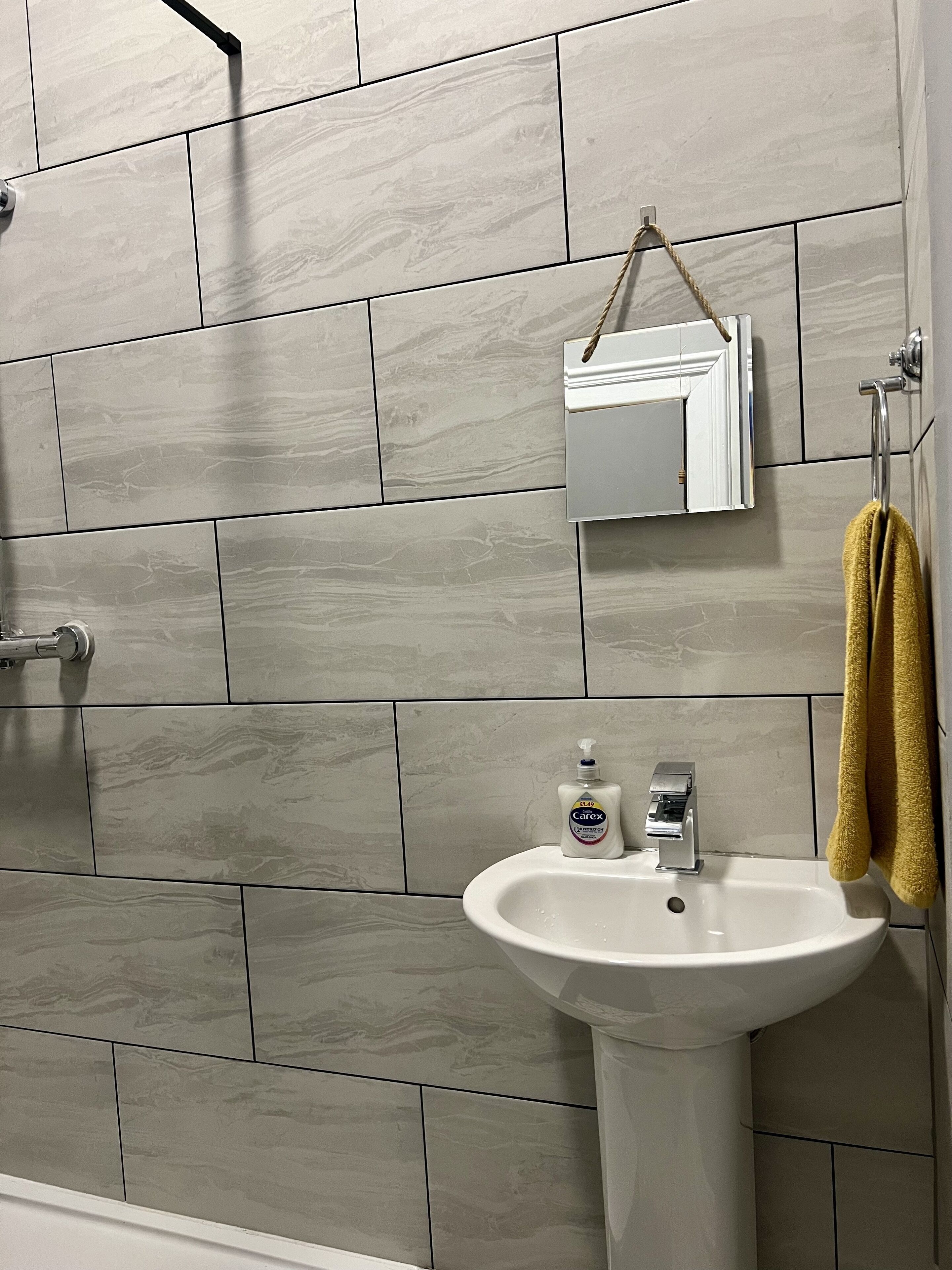 A bathroom with a white sink, a bottle of hand soap, and a towel hanging on a rack.