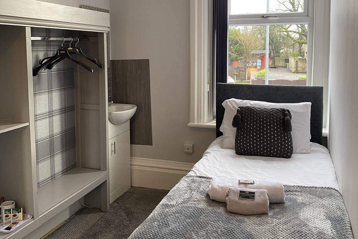 Une chambre à coucher avec un lit, une fenêtre avec des rideaux, une armoire et un lavabo.