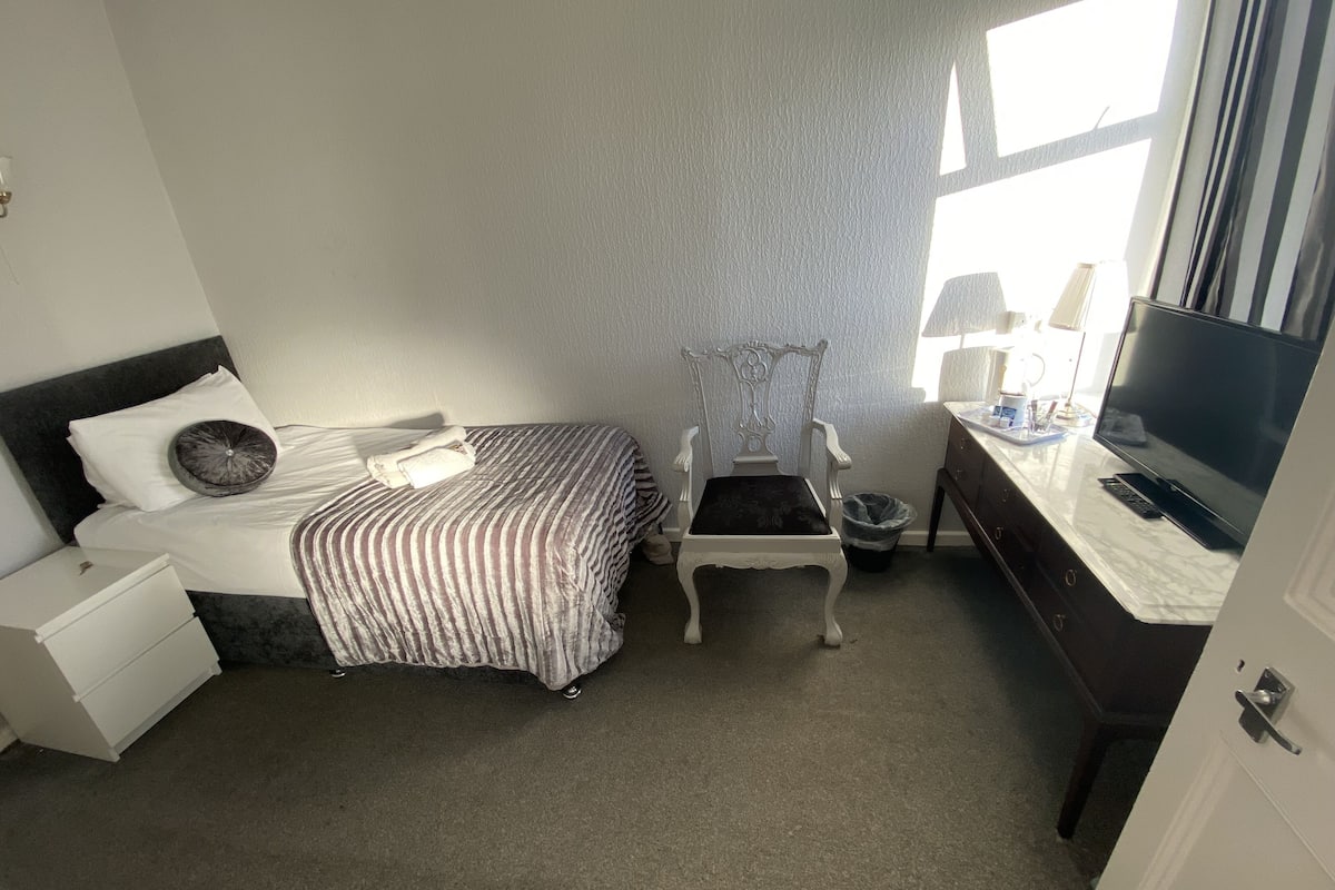 Une chambre d’hôtel avec un lit, une chaise, un bureau avec un ordinateur et une télévision.