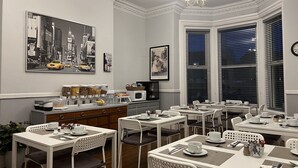 A dining area with white tables and chairs, a coffee station, and artwork on the walls. - St Andrews House Hotel (Preston)