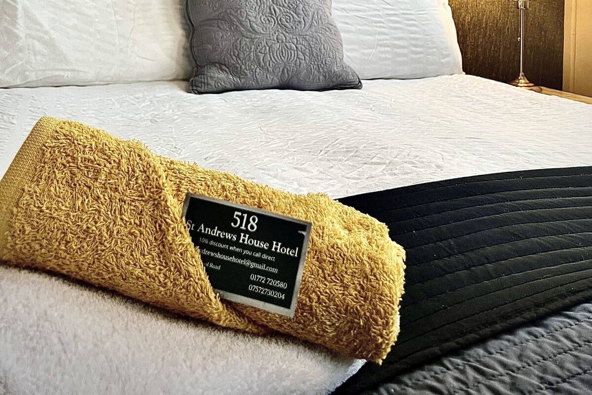 Une chambre d’hôtel avec un lit, une œuvre d’art représentant une carte du monde, une lampe et un panneau posé sur le lit.