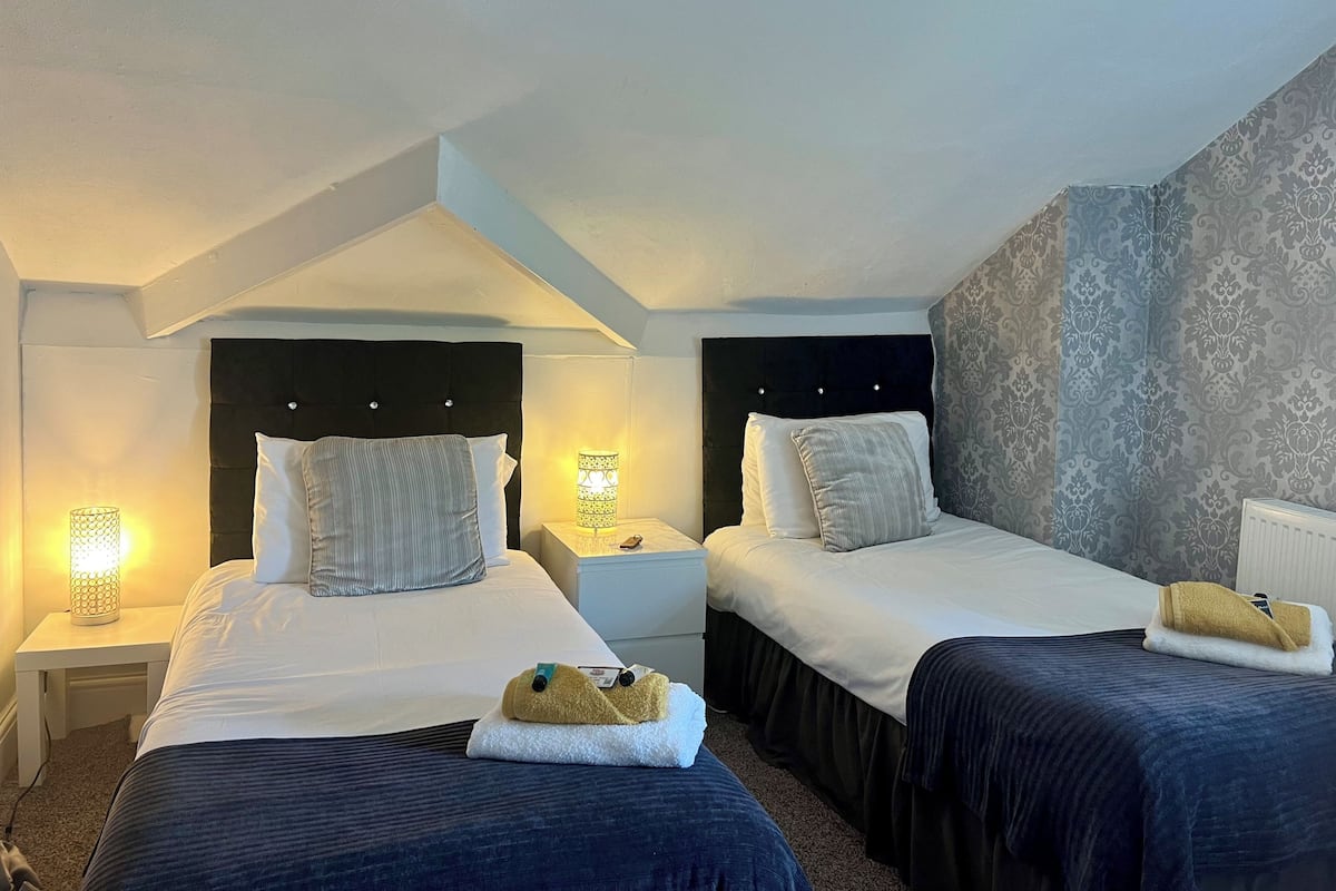 Une chambre d’hôtel avec deux lits, chacun doté d’une tête de lit, de lampes de chevet et d’une petite table.