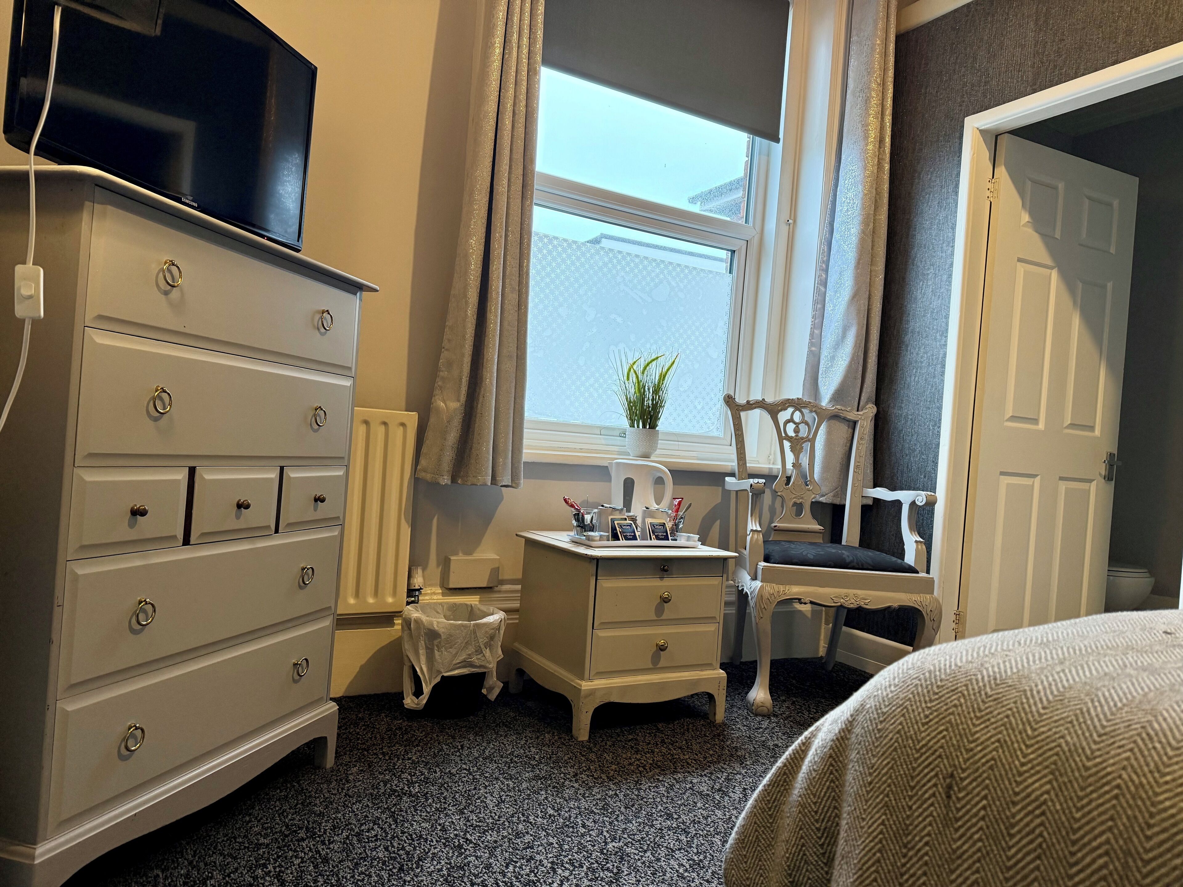 A bedroom with a dresser, a vanity, a chair, and a window with curtains.