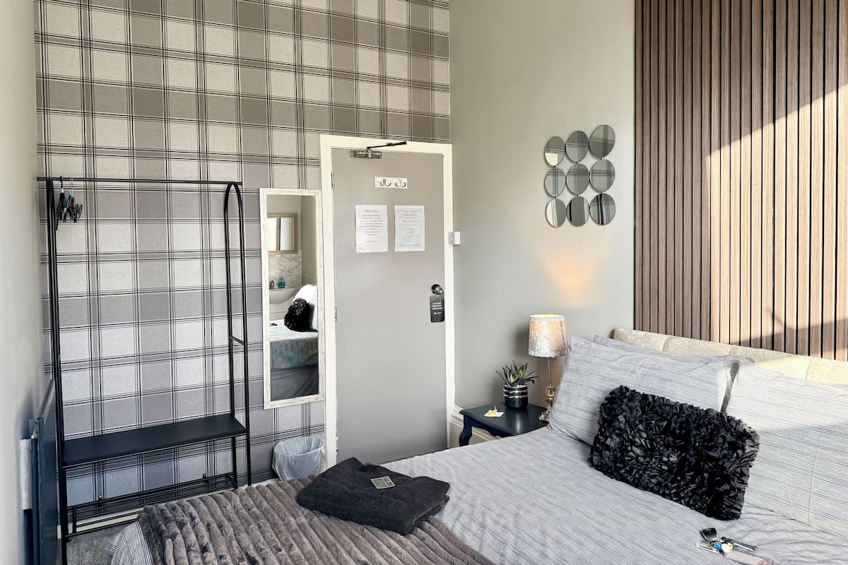 Une chambre moderne avec un lit, une table de chevet avec une lampe, un miroir fixé au mur et une porte avec une serrure.