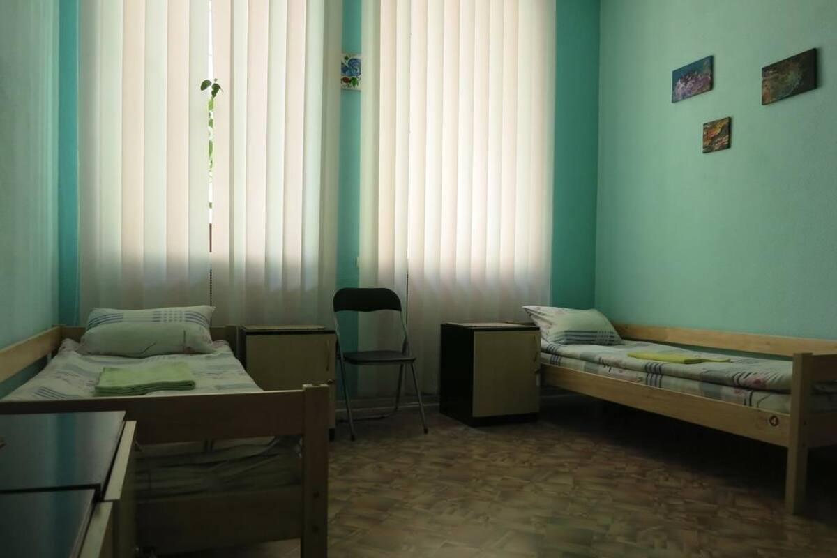 Quarto em dormitório com duas camas, uma escrivaninha, uma cadeira e uma mesa pequena.