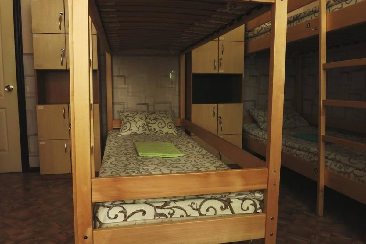 Uma cama de solteiro com colcha estampada, cabeceira de madeira e uma toalha verde. Existem duas camas beliche de madeira em ambos os lados.