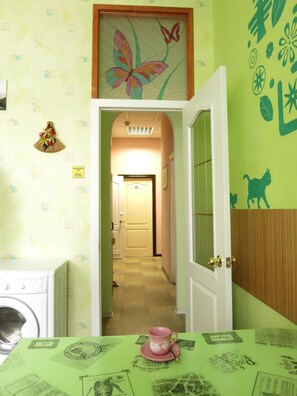 A room with a green wall, a framed butterfly artwork, a door leading to another room, and a table with a pink cup. - Hostel Delil (Kyiv)