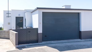 En modern byggnad med en stor garageport, en grind vid ingången och ett litet fönster.