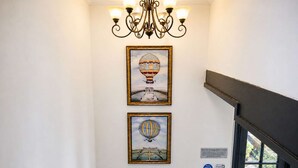 A hallway with two framed artworks depicting hot air balloons, a chandelier, and a door with a sign. - Falstaff Cottage - Sleeps up to 5 - Stratford upon Avon (Stratford upon Avon)