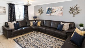 A living room with a dark brown leather sectional sofa, patterned throw pillows, a decorative rug, and wall art. - Falstaff Cottage - Sleeps up to 5 - Stratford upon Avon (Stratford upon Avon)