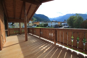 A wooden balcony with a view of a mountain range and buildings in the background.