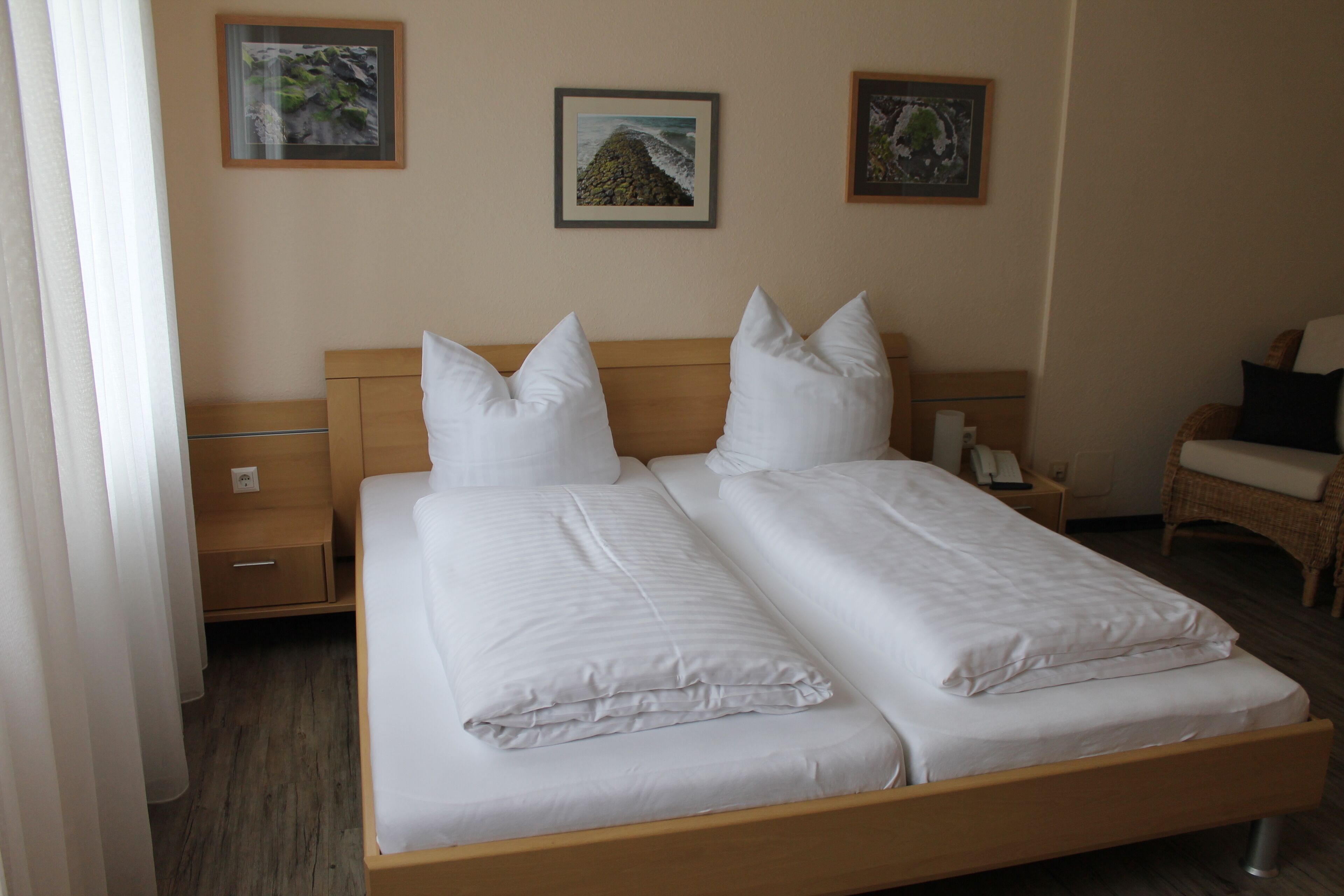 Un lit double avec du linge de lit blanc, une tête de lit en bois et deux tables de chevet avec des lampes.