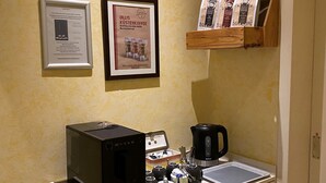 A kitchenette with a coffee maker, a toaster, and a microwave on a counter. There are framed pictures on the wall and a shelf with coffee bags. - Alleehotel Eschen (Aurich)