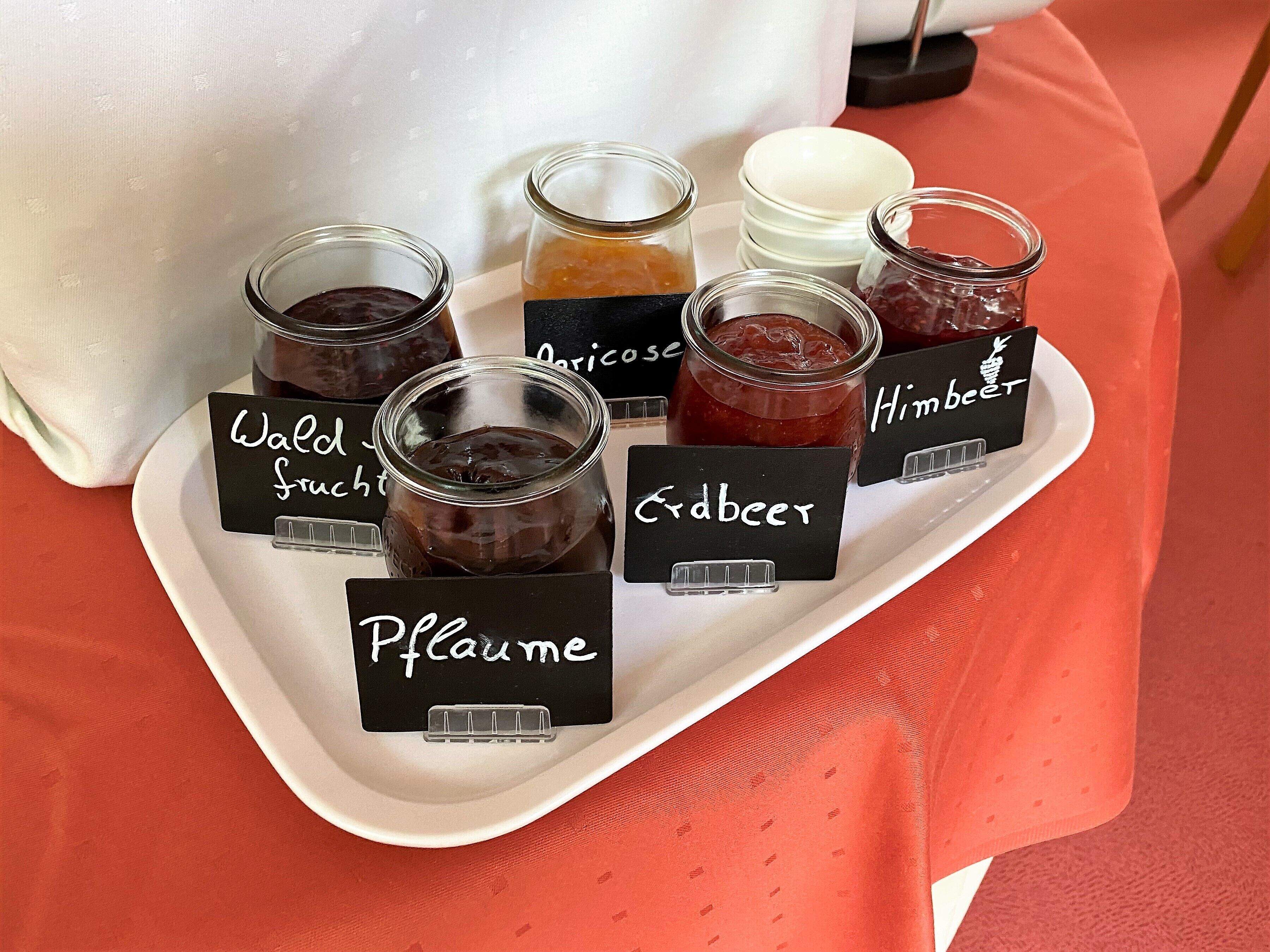 Un plateau contenant des pots de confiture étiquetés avec des noms tels que « Wall Frucht », « Erdbier » et « Himbeet ».