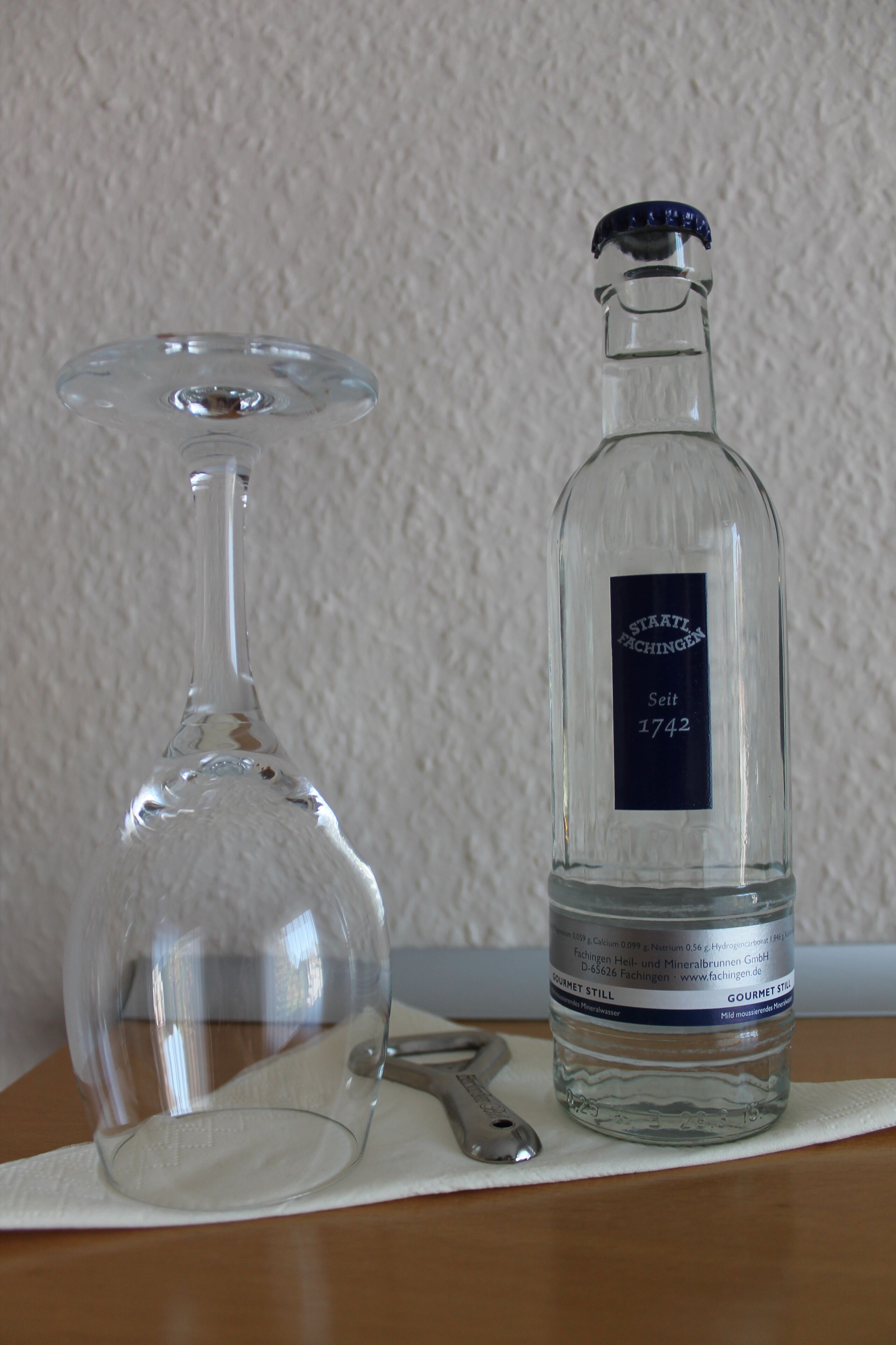 A clear glass bottle and a wine glass on a white cloth.