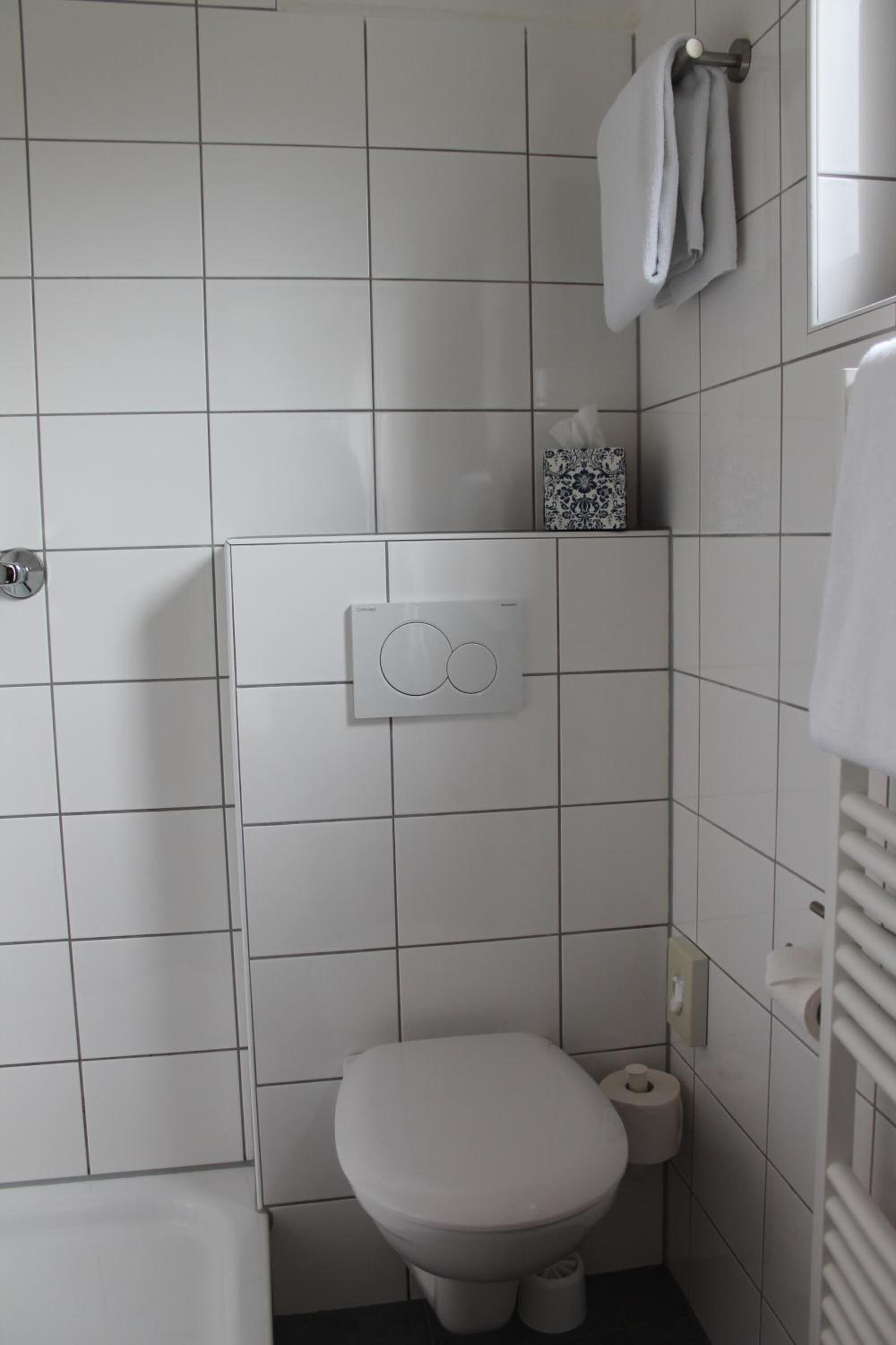 Um banheiro pequeno e moderno, com azulejos brancos, vaso sanitário, bidê e porta-toalhas.