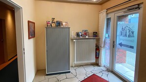 A hotel lobby with a red carpet, a radiator, and a glass door leading outside. - Alleehotel Eschen (Aurich)