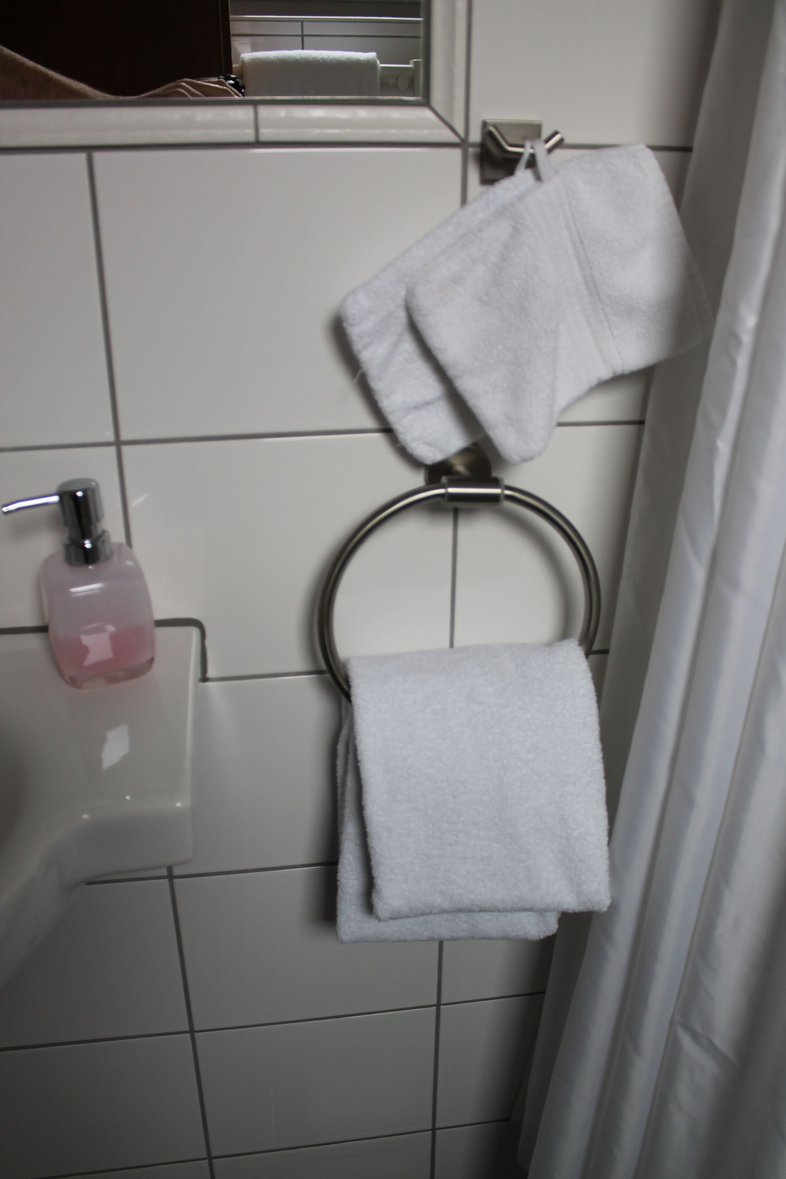 A bathroom with a white sink, a soap dispenser, a towel ring with a folded towel, and a shower curtain.