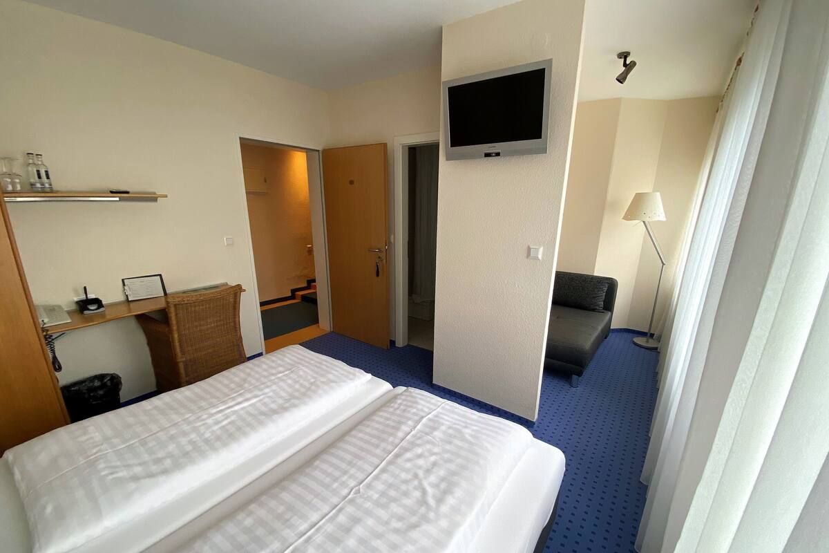 Une chambre d’hôtel comprenant un lit, un téléviseur fixé au mur, un bureau avec une lampe et un canapé.