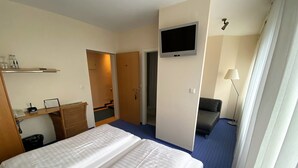 A hotel room with a bed, a TV mounted on the wall, a desk with a lamp, and a sofa. - Alleehotel Eschen (Aurich)