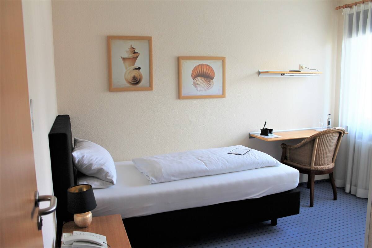 Une chambre d’hôtel avec un lit, un bureau, une chaise, une lampe et deux tableaux encadrés au mur.
