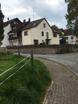 Ein zweistöckiges Wohngebäude mit Balkon, einer kleinen Veranda und einer Steinmauer.